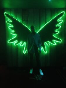 Image of man standing in front of neon wings.